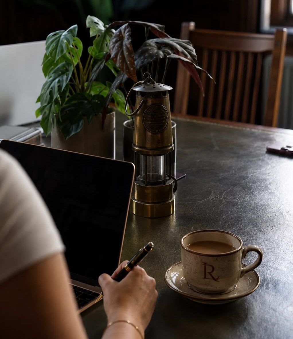 Woman working on laptop with Davy lamp and Lamproom branded coffee cup on desk